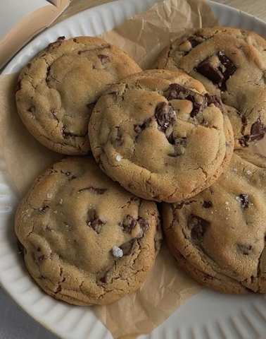 Five chocolate chip cookies stacked on a white plate