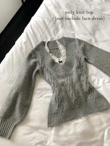 Grey cable knit V-neck sweater laid on a bed